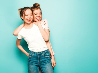 İki güzel sarışın, gülümseyen yenilikçi kız, son moda hippi kot pantolon giyiyorlar. Mavi duvarın yanında poz veren kaygısız seksi kadınlar. Moda ve pozitif modeller eğleniyor.