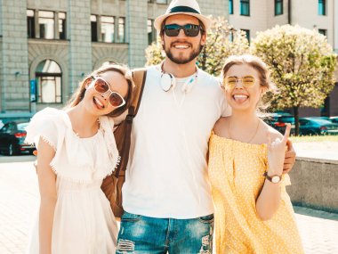 Sokakta poz veren üç genç arkadaş grubu. Moda adamı ve sıradan yaz kıyafetleri giymiş iki tatlı kız. Gülümseyen mankenler güneş gözlükleriyle eğleniyorlar. Neşeli kadınlar ve erkekler çıldırıyor.