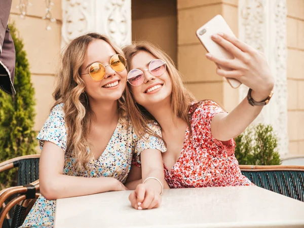 流行の夏の太陽の下で2人の若い美しい笑顔のヒップスターの女の子 ストリートの背景にベランダカフェでおしゃべりケアフリー女性 — ストック写真