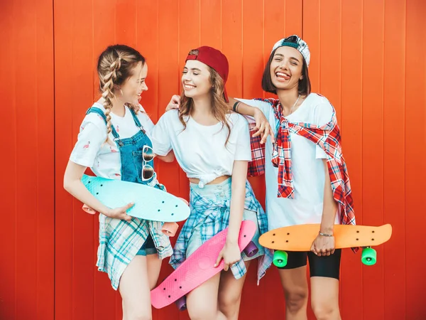 カラフルなペニースケートボードを持つ3人の若い笑顔の美しい女の子 赤い壁の近くの通りにポーズ夏のヒップスター服の女性 — ストック写真