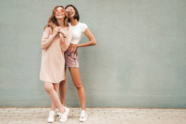 Son moda yaz kıyafetleri içinde iki güzel gülümseyen hippi kız. Güneş gözlükleriyle sokak arka planında poz veren kaygısız kadınlar. Pozitif modeller eğleniyor ve sarılıyorlar.