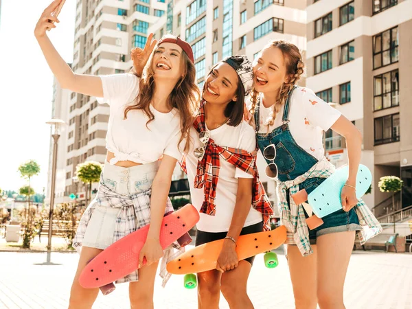 カラフルなペニースケートボードを持つ3人の若い笑顔の美しい女の子 路上でポーズをとる夏のヒップスター服の女性たち 自撮り自画像を撮影したポジティブモデル — ストック写真