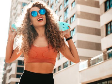 Kıvırcık saçlı, genç, güzel, seksi, tebessüm eden hippi kadın. Yazlık elbiseli, modaya uygun, sokakta poz veren, mavi kuruşlu kaykaylı kadın.