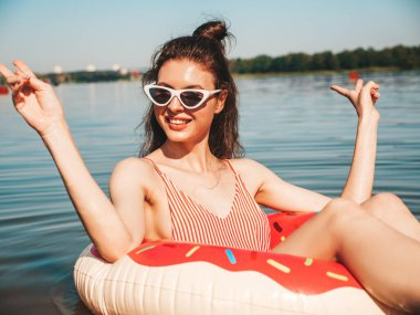 Güneş gözlüklü genç, güzel, seksi hippi kadın. Mayo giyen kız mayo giyiyor, yüzüyor ve lilo şişirilebilir şilteler içinde yatıyor. Gölde dinlenen pozitif kadın.