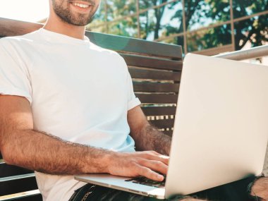 Yakışıklı, güler yüzlü, stil sahibi hipster Lambersex modeli. Moda adamı sokakta bankta oturuyor ve dizüstü bilgisayar kullanıyor, mesaj yazıyor. Ortak çalışma konsepti. Teknoloji ve iletişim