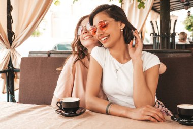 Son moda yaz kıyafetleri içinde gülümseyen iki genç hippi kız. Veranda kafesinde sohbet eden ve kahve içen kaygısız kadınlar. Pozitif modeller eğleniyor ve iletişim kuruyor.