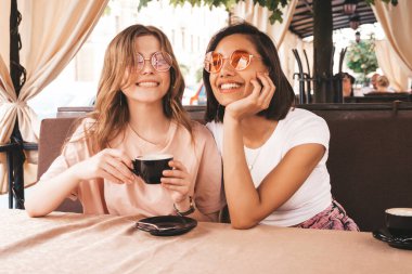 Son moda yaz kıyafetleri içinde gülümseyen iki genç hippi kız. Veranda kafesinde sohbet eden ve kahve içen kaygısız kadınlar. Pozitif modeller eğleniyor ve iletişim kuruyor.