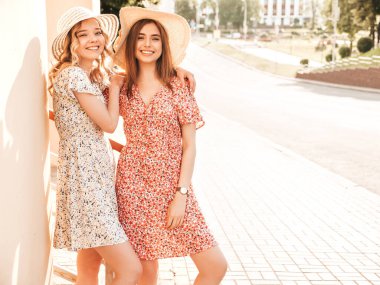 İki güzel gülümseyen yeniyetme kız şık yaz kıyafetleri içinde sokakta şapkalarla poz veren kaygısız kadınlar. Pozitif modeller eğleniyor ve sarılıyorlar.