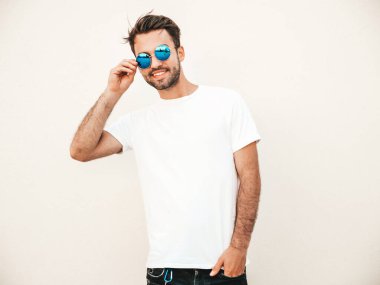 Yakışıklı, gülümseyen stil sahibi Lambersex modelinin portresi. Beyaz tişört giyen adam. Moda erkeği, yuvarlak güneş gözlükleriyle duvarın yanında sokak arkasında poz veriyor.