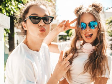 Son moda beyaz tişörtlü iki güzel gülümseyen hippi kızın portresi. Sokakta poz veren kaygısız kadınlar. Pozitif modeller eğleniyor, sarılıyor ve deliriyor.