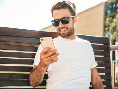 Yakışıklı, şık, havalı, lamberseksüel bir model. Beyaz tişört giymiş bir adam. Sokakta poz veren bir erkek. Cep telefonunda tutuyor, kaydırıyor ve mesaj atıyor. Akıllı telefondan mesaj yazar