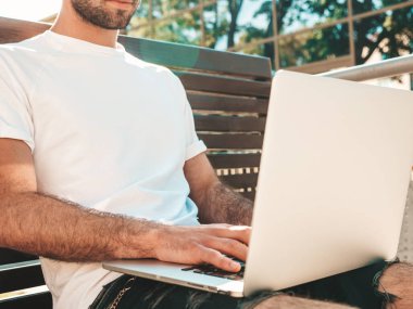 Yakışıklı, güler yüzlü, stil sahibi hipster Lambersex modeli. Moda adamı sokakta bankta oturuyor ve dizüstü bilgisayar kullanıyor, mesaj yazıyor. Ortak çalışma konsepti. Teknoloji ve iletişim