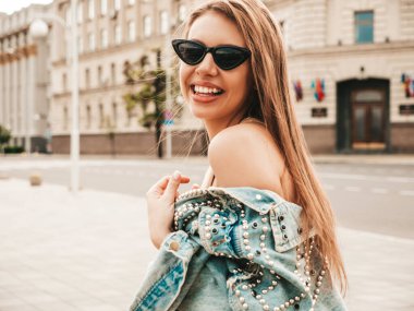 Hipster kot ceket giymiş güzel gülümseyen bir modelin portresi. Sokakta poz veren modaya uygun bir kız. Komik ve pozitif kadın güneş gözlükleriyle eğleniyor.