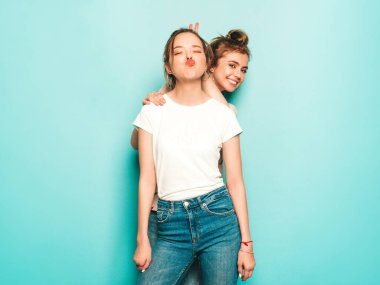 İki güzel sarışın, gülümseyen yenilikçi kız, son moda hippi kot pantolon giyiyorlar. Mavi duvarın yanında poz veren kaygısız seksi kadınlar. Moda ve pozitif modeller eğleniyor.