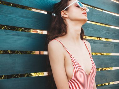 Güneş gözlüklü, sokakta çitin yanında poz veren genç, güzel, rahat, hippi bir kadın. Yazın mayo giyen moda bir kız. Pozitif kadın deliriyor. Komik model. 