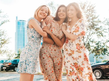 Üç güzel gülümseyen yeniyetme kız şık yaz kıyafetleri içinde. Sokakta poz veren kaygısız kadınlar. Pozitif mankenler eğleniyor ve sarılıyorlar. Alışverişten sonra yürüyorlar.