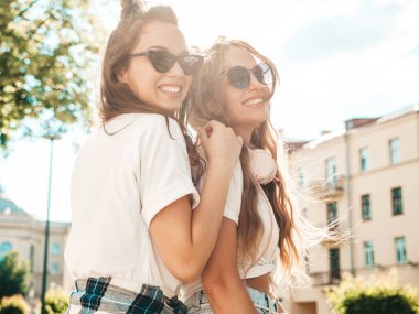 Son moda beyaz tişörtlü iki güzel gülümseyen hippi kadının portresi. Sokakta poz veren kaygısız kadınlar. Pozitif modeller eğleniyor, sarılıyor ve deliriyor.