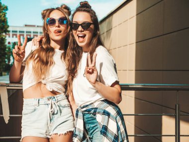 Son moda beyaz tişörtlü iki güzel gülümseyen hippi kadının portresi. Sokakta poz veren kaygısız kadınlar. Pozitif modeller eğleniyor, sarılıyor ve deliriyor.
