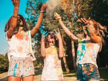 Yaz mevsiminde Holi Renk Festivali 'nde parti veren üç mutlu güzel kız. Gün batımında müzik etkinliğinden sonra gülümseyen genç bayan arkadaşlar eğleniyor. Güneş batarken güneş gözlükleriyle çıldıran pozitif modeller.