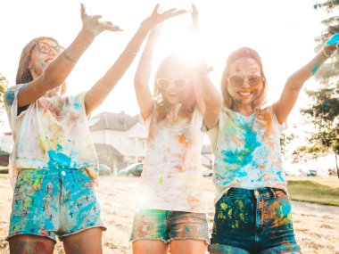Yaz mevsiminde Holi Renk Festivali 'nde parti veren üç mutlu güzel kız. Gün batımında müzik etkinliğinden sonra gülümseyen genç bayan arkadaşlar eğleniyor. Güneş batarken güneş gözlükleriyle çıldıran pozitif modeller.