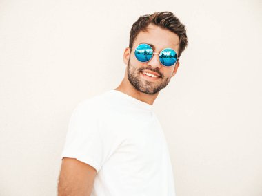 Yakışıklı, kendine güvenen, stil sahibi, Lambersex mankeni portresi. Beyaz tişört giyen adam. Moda erkek, dışarıda güneş gözlüklü, duvarın yanında poz veriyor.