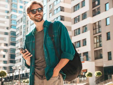 Yakışıklı, şık, havalı, lamberseksüel bir model. Beyaz tişört giymiş bir adam. Sokakta poz veren bir erkek. Cep telefonunda tutuyor, kaydırıyor ve mesaj atıyor. Akıllı telefondan mesaj yazar