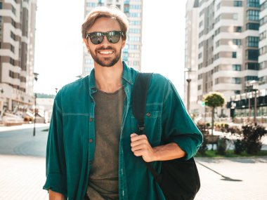 Yakışıklı, gülümseyen stil sahibi Lambersex modelinin portresi. Yeşil tişörtlü adam. Moda erkeği güneş gözlükleriyle gökdelende poz veriyor. Gün batımında dışarıda yürüyor. 