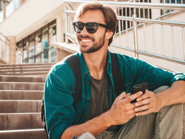 Yakışıklı, şık, havalı, lamberseksüel bir manken. Beyaz tişört giymiş bir adam. Merdivenlerde oturan moda bir erkek. Cep telefonunda tutuyor, kaydırıyor ve mesaj atıyor. Akıllı telefondan mesaj yazar