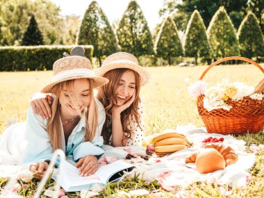 İki güzel gülümseyen yeniyetme yaz elbisesi ve şapkalı kız. Piknik yapan kaygısız kadınlar. Çimlerin üzerinde oturan, kitap okuyan, meyve ve peynir yiyen pozitif modeller.