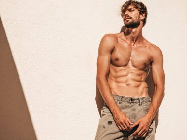 Yakışıklı, güçlü bir adamın portresi. Kot pantolonla beyaz duvarın yanında poz veren sağlıklı atletik fitness modeli. Çıplak gövdesi olan kendine güvenen seksi moda erkeği. Lamberseksüel açık hava