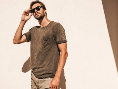 Yakışıklı, kendine güvenen, stil sahibi, Lambersex mankeni portresi. Tişört giymiş adam. Moda erkek, güneş gözlüklü beyaz duvarın yanında poz veriyor.