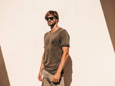 Yakışıklı, kendine güvenen, stil sahibi, Lambersex mankeni portresi. Tişört giymiş adam. Moda erkek, güneş gözlüklü beyaz duvarın yanında poz veriyor.