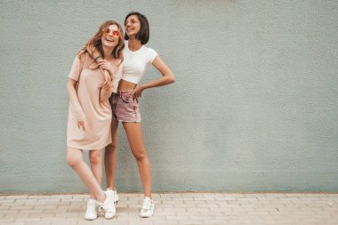Son moda yaz kıyafetleri içinde iki güzel gülümseyen hippi kız. Güneş gözlükleriyle sokak arka planında poz veren kaygısız kadınlar. Pozitif modeller eğleniyor ve sarılıyorlar.