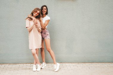 Son moda yaz kıyafetleri içinde iki güzel gülümseyen hippi kız. Güneş gözlükleriyle sokak arka planında poz veren kaygısız kadınlar. Pozitif modeller eğleniyor ve sarılıyorlar.