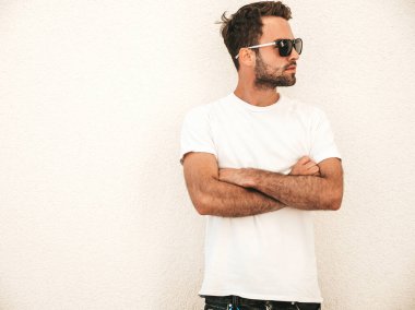 Yakışıklı, kendine güvenen, stil sahibi, Lambersex mankeni portresi. Beyaz tişört giyen adam. Moda erkek, dışarıda güneş gözlüklü, duvarın yanında poz veriyor. Çapraz kollar