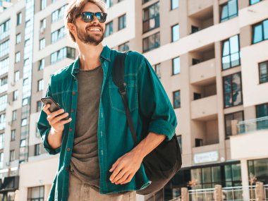 Yakışıklı, şık, havalı, lamberseksüel bir model. Tişört giymiş bir adam. Beyaz duvarın yanında sokakta poz veren bir erkek. Cep telefonunda tutuyor, kaydırıyor ve mesaj atıyor. Akıllı telefondan mesaj yazar