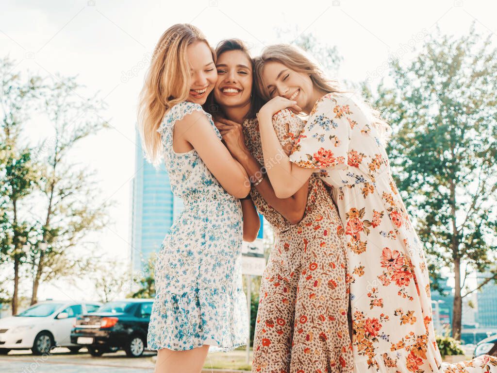 Three young beautiful smiling hipster girls in trendy summer sundress.Sexy carefree women posing on the street background. Positive models having fun and hugging.Walking after shopping