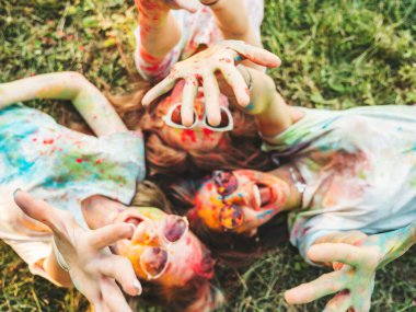 Yaz mevsiminde Holi Renk Festivali 'nde parti veren üç mutlu güzel kız. Gün batımında müzik etkinliği sonrasında gülümseyen genç bayan arkadaşlar. Güneş gözlüklü mankenler çimlerin üzerinde yatıyor.
