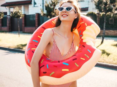 Güneş gözlüklü genç, güzel, seksi hippi kadın. Yaz mayosu giymiş, şişme donutlu kadın. Sokakta poz veren kadın. 
