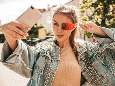 Hipster kot ceketli güzel bir mankenin portresi. Karpuz şekeri yiyen kız. Sokakta poz veren bir kadın. Güneş gözlüklü bir kadın. Selfie çekiyor.