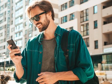 Yakışıklı, şık, havalı, lamberseksüel bir model. Tişört giymiş bir adam. Beyaz duvarın yanında sokakta poz veren bir erkek. Cep telefonunda tutuyor, kaydırıyor ve mesaj atıyor. Akıllı telefondan mesaj yazar