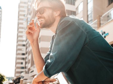 Yakışıklı, gülümseyen stil sahibi Lambersex modelinin portresi. Yeşil tişörtlü adam. Moda erkek gökdelenin arkasında güneş gözlükleriyle poz veriyor.