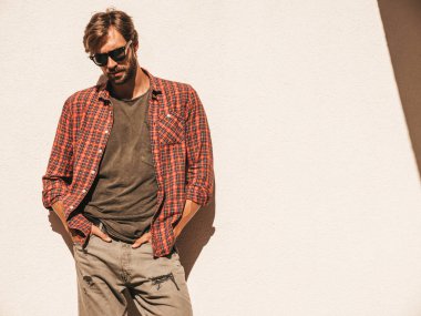 Yakışıklı, şık bir hipster Lambersex mankeni portresi. Kareli gömlek giymiş bir adam. Moda erkek, güneş gözlüklü beyaz duvarın yanında poz veriyor.