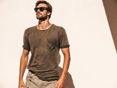 Yakışıklı, kendine güvenen, stil sahibi, Lambersex mankeni portresi. Tişört giymiş adam. Moda erkek, güneş gözlüklü beyaz duvarın yanında poz veriyor.