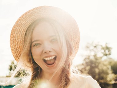 Moda bir yaz elbisesi içinde gülümseyen güzel hippi kız portresi. Günbatımında şapkayla parkta sokakta poz veren kaygısız seksi kadın. Açık havada pozitif model.