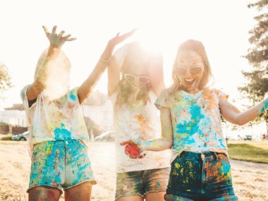 Yaz mevsiminde Holi Renk Festivali 'nde parti veren üç mutlu güzel kız. Gün batımında müzik etkinliğinden sonra gülümseyen genç bayan arkadaşlar eğleniyor. Güneş batarken güneş gözlükleriyle çıldıran pozitif modeller.