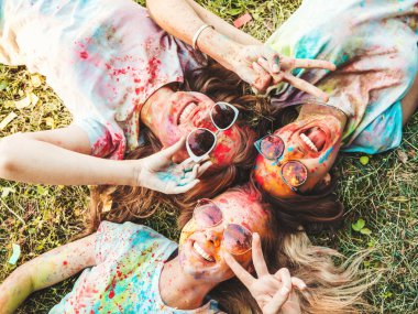Yaz mevsiminde Holi Renk Festivali 'nde parti veren üç mutlu güzel kız. Gün batımında müzik etkinliği sonrasında gülümseyen genç bayan arkadaşlar. Güneş gözlüklü mankenler çimlerin üzerinde yatıyor.