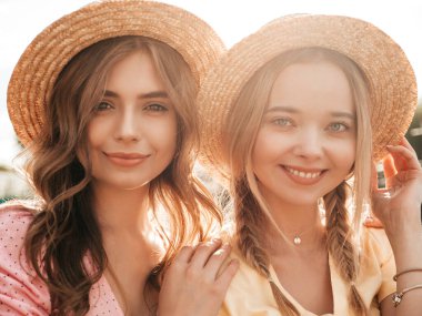 İki genç, güzel, gülümseyen yeniyetme kadın, modaya uygun bir yaz elbisesi içinde. Parkta şapkalarla poz veren kaygısız seksi kadınlar. Pozitif modeller gün batımında eğleniyor ve sarılıyorlar.