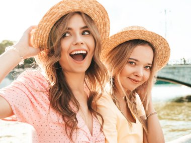 İki genç, güzel, gülümseyen yeniyetme kadın, modaya uygun bir yaz elbisesi içinde. Sokakta arka planda şapkalı setin yanında poz veren seksi kaygısız kadınlar. Pozitif modeller eğleniyor ve sarılıyorlar.