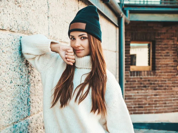 美丽的微笑模型的肖像 穿着保暖的嬉皮士白色毛衣和便帽的女性 一个时髦的女孩在街上靠墙站着 在户外玩乐的有趣而积极的女人 — 图库照片